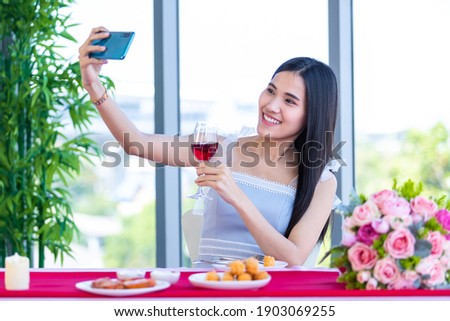 Valentine's day concept,Selfie of Happy of smiling Asian young female sitting at a table food holding with wine glasses at in the restaurant background