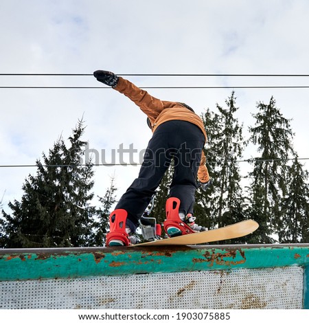 Rear view of leaned snowboarder trying to keep balance, low angle view. Sportsman wearing colorful vivid ski suit, red boots and snowboard. Concept of freeride
