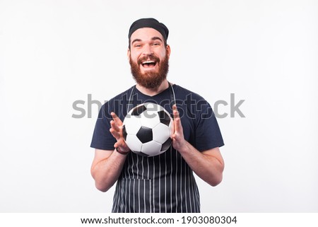 Cheerful young chef man holding soccer ball over white background