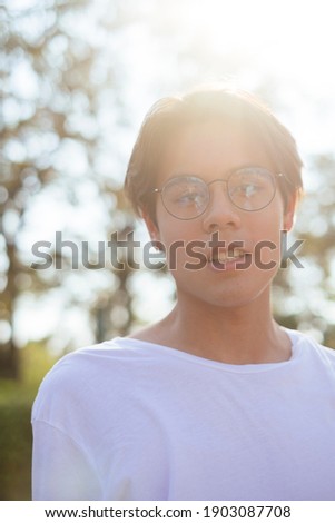Medium close up silhouette shot of black hair guy in white t-shirt and eyeglasses in the park.