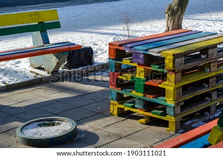Modern street art concept. A seating area on a city street made of multicolored pallets. Colorful benches and table. Sunny winter day. No people.