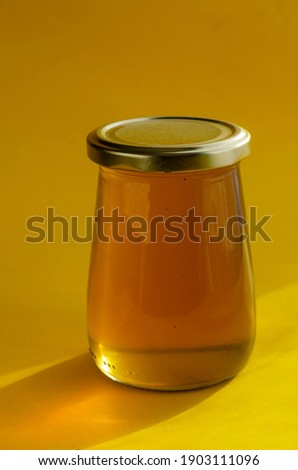 Natural sugar substitute, healthy food concept. Raw bee honey in glass jar on yellow background.  Close-up of liquid organic honey. Selective focus.