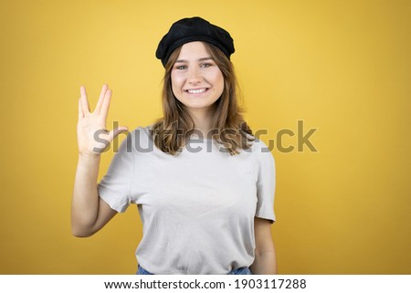 Beautiful young caucasian girl wearing french look with beret over isolated yellow background doing hand symbol