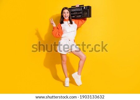 Full length photo portrait of woman showing v-sign with boombox on shoulder isolated on vivid yellow colored background