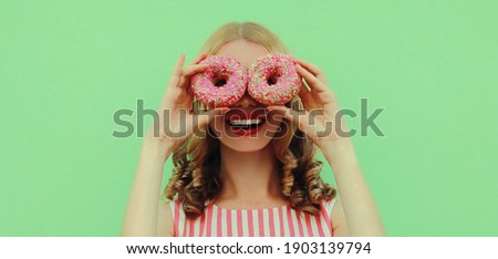 Portrait close up of happy smiling young woman with two donuts having fun on a green background