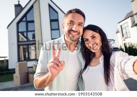 Photo portrait of happy family couple wife husband showing v-sign smiling outside new home after moving relocating