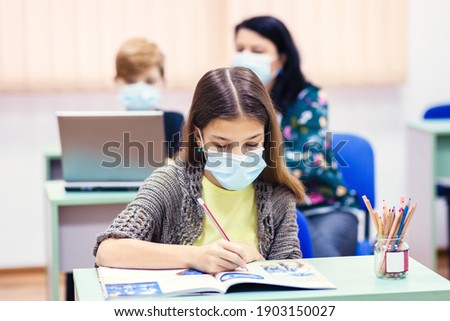 Children with face mask back to school in classroom after covid-19 lockdown - Teacher helping kid to use computer doing hybrid education class after school reopening Royalty-Free Stock Photo #1903150027