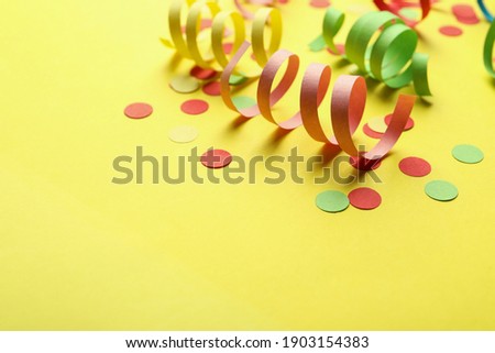 Colorful serpentine streamers and confetti on yellow background. Space for text