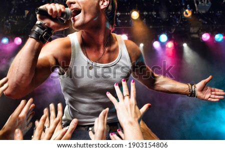 Male singer on stage with fans trying to grab him