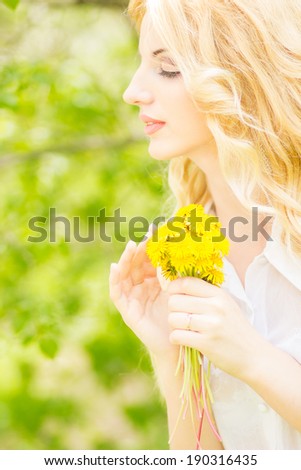 Portrait of a beautiful young blonde woman with dandelions. Girl posing in nature and smiling