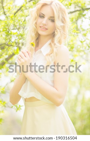 Portrait of a beautiful young blonde woman with dandelions. Girl posing in nature and smiling