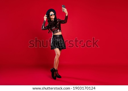 Photo of charming girl hold telephone take selfie wear glossy top cap leather mini skirt sunglass isolated red color background