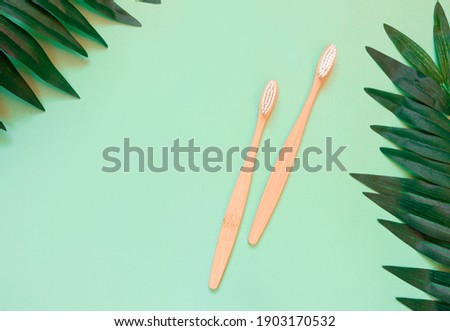 Two wooden bamboo eco friendly toothbrushes and tropical green leaves on a green background. Waste concept without plastic. Flat lay, top view, copy space for text
