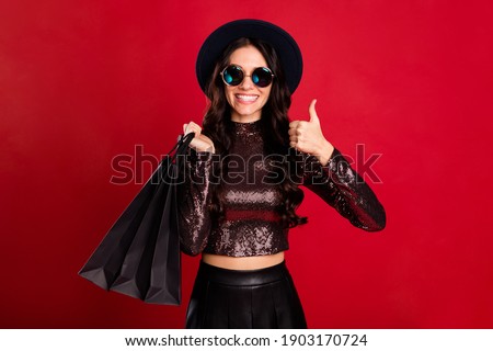 Portrait of cheerful curly hairstyle person hold bags show thumb up toothy smile isolated on red color background