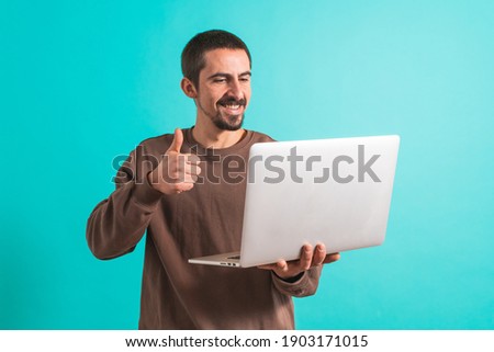 Young handsome man with his laptop computer talking via video call isolated over blue background. Happy male enjoying music.