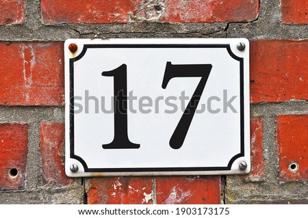 A white house number plaque, showing the number seventeen (17)  Royalty-Free Stock Photo #1903173175