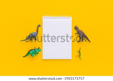 notepad or copybook and toys dinosaurs on a colored yellow background. minimalistic composition, top view, flat lay, mock up