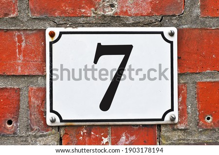 A white house number plaque, showing the number seven (7) 