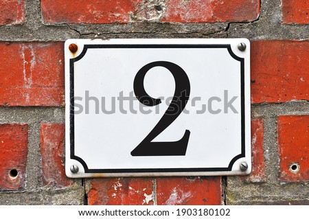 A white house number plaque, showing the number two (2)