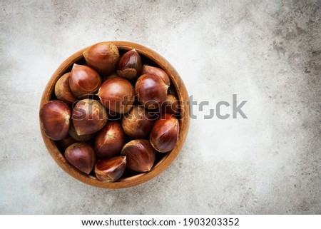 Pile of fresh sweet chestnuts in a bamboo bowl over grey background. Flat lay, copy space Royalty-Free Stock Photo #1903203352