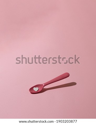 Pink , plastic spoon with heart on pink pastel background. Creative, minimal concept.
