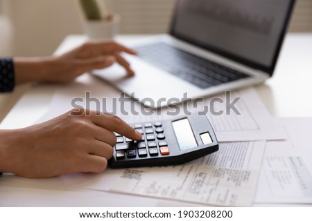 Close up of young female electronic bank client using calculator in paperwork with accounts bills before providing payment online by laptop. Woman hands at work table with papers accounting sum to pay Royalty-Free Stock Photo #1903208200