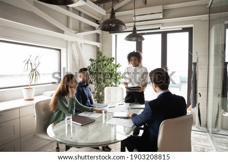Confident African American businesswoman leading briefing, explaining strategy, training diverse staff sitting at table in boardroom, group negotiations, business partners sharing startup ideas Royalty-Free Stock Photo #1903208815