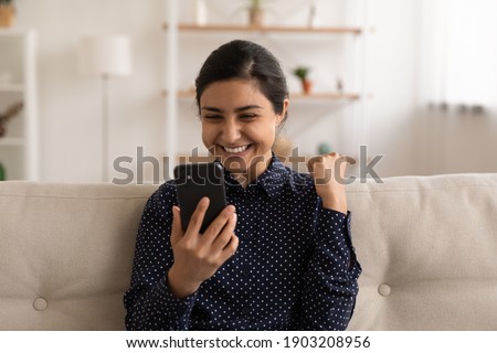 Overjoyed millennial indian woman client receive perfect discount proposition from internet shop. Excited young mixed race female read good news on cell get loan approval from bank credit organization Royalty-Free Stock Photo #1903208956