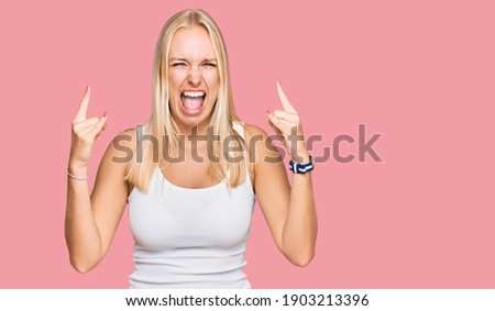 Young blonde girl wearing casual style with sleeveless shirt shouting with crazy expression doing rock symbol with hands up. music star. heavy music concept. 