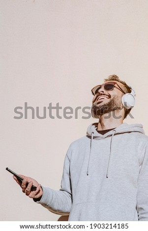 Young man laughing as he looks at his phone and listens to music with a neutral background.