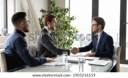 Happy business partners shaking hands, greeting or making successful great commercial deal after successful negotiations, smiling diverse employees sitting at table in modern boardroom, acquaintance Royalty-Free Stock Photo #1903216519