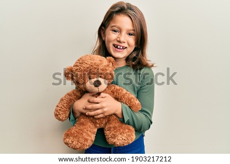 Little beautiful girl hugging teddy bear smiling and laughing hard out loud because funny crazy joke.  Royalty-Free Stock Photo #1903217212