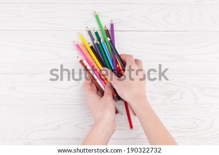 Colour pencils in hands on white wooden background