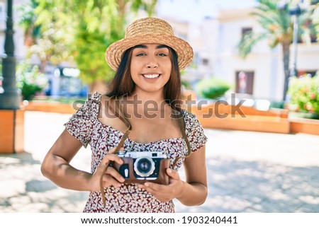 Young latin woman on vacation using vintage camera walking at street of city.