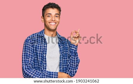 Young handsome african american man wearing casual clothes with a big smile on face, pointing with hand and finger to the side looking at the camera. 
