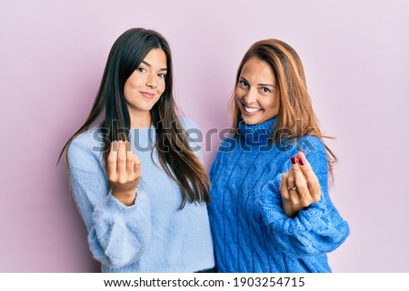Hispanic family of mother and daughter wearing wool winter sweater doing money gesture with hands, asking for salary payment, millionaire business 
