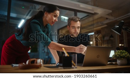 Handsome Young Project Manager and Beautiful Creative Director Work and Talk About Business Strategy on a Laptop Computer in Creative Office. Life of a Busy Marketing Agency in Modern Loft Building. Royalty-Free Stock Photo #1903260661
