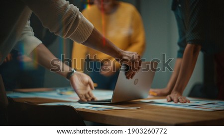 Close Up of Diverse Multiethnic Team Having Conversation in Meeting Room in a Creative Office. Colleagues Lean On a Conference Table, Look at Laptop Computer and Make Notes with Pencils on Notebooks. Royalty-Free Stock Photo #1903260772