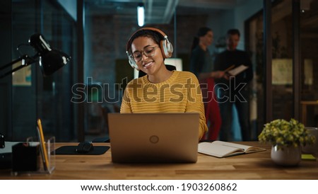 Young Hispanic Project Manager in Headphones and Working on Laptop Computer in Busy Creative Office Environment. Beautiful Diverse Multiethnic Female Specialist is Writing Business Strategy. Royalty-Free Stock Photo #1903260862