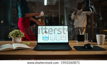 Shot of a Laptop Computer Standing on a Desk in a Busy Creative Office Environment. Display Shows Development of Food Delivery App User Interface. Authentic Hipster Agency Vibe. Royalty-Free Stock Photo #1903260871