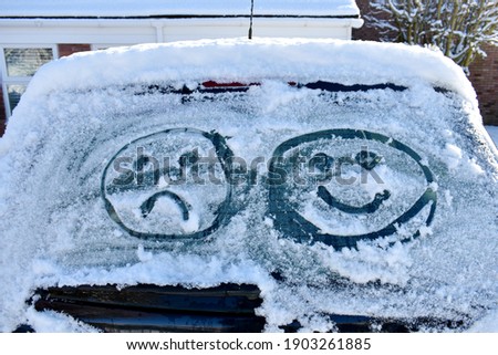 close up of car screen covered in snow with two emoji faces drawn into ice, one happy and one sad. outside on a cold sunny winter's day Royalty-Free Stock Photo #1903261885