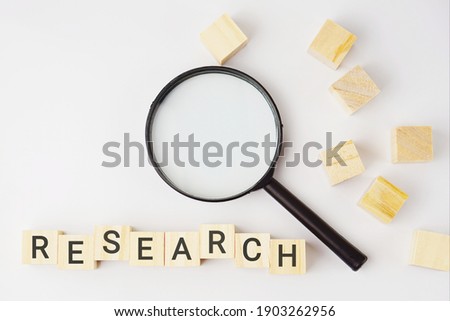 Selective focus of wooden cubes with wording "RESEARCH" and magnifying glass on a white background. Business, strategy and education concept. This photo contains noise and grain.