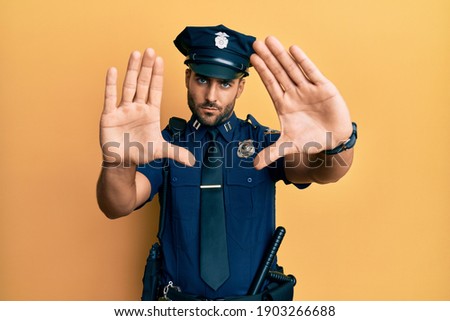 Handsome hispanic man wearing police uniform doing frame using hands palms and fingers, camera perspective 