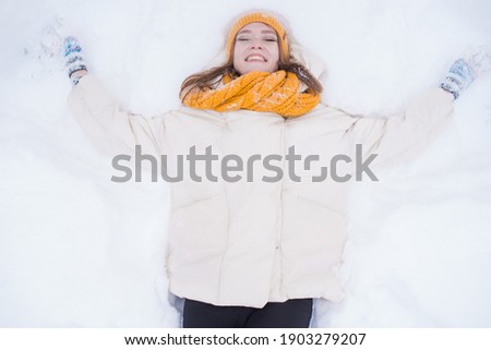 Portrait of a happy smiling girl lying on the snow on a snowy winter day