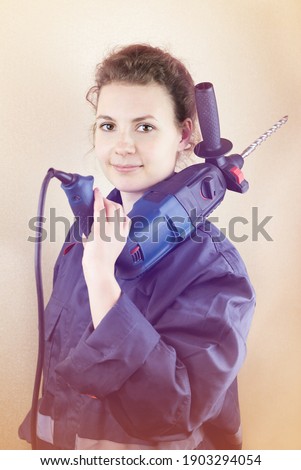 Smiling beautiful woman in workwear with a puncher near the wall, toned photo.