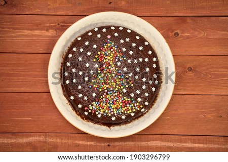 CAKE. chocolate cake decorated with a Christmas tree and white snowflakes. on a white plate. on a wooden background. Christmas and New Years concept. top view