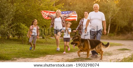 big family are walking walking american flags. Front view, american patriots on the park meadow.