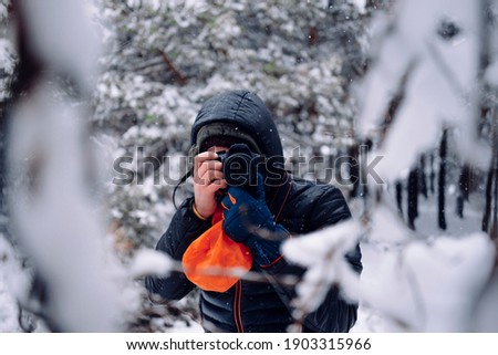 A caucasian unrecognizable photographer man hidden in a forest full of snow in winter time