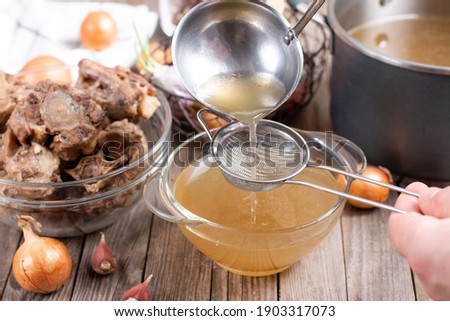 Passing the bone broth through a sieve. Concentrated Bone Broth in a bowl
