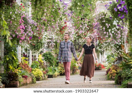 A young couple walks in the garden or park. holding hands. Blooming colorful flowers, relaxed summer leisure. Love is in the air. Small talk, nice aromas, romantic mood. Happy boy and girl. Wide shot.